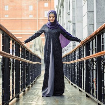 Woman in a hijab standing on a walkway with outstretched arms.
