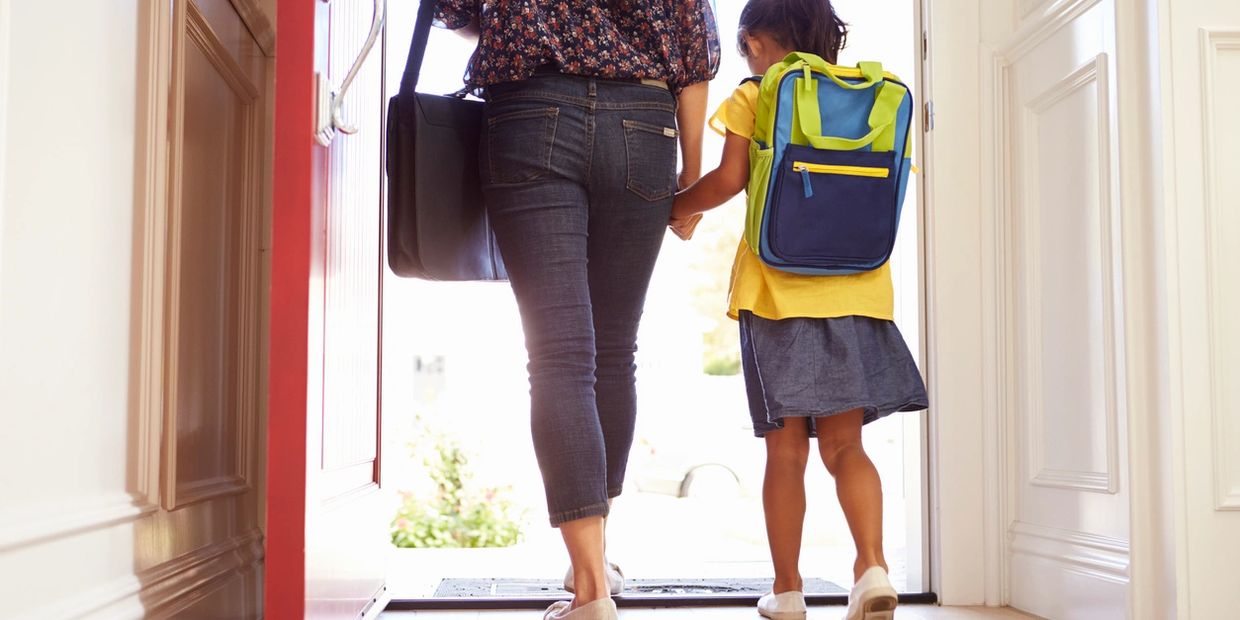 Parent and child holding hands, walking out the door with a backpack.