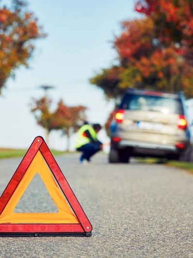 Warning triangle placed on road with a car and person in background.