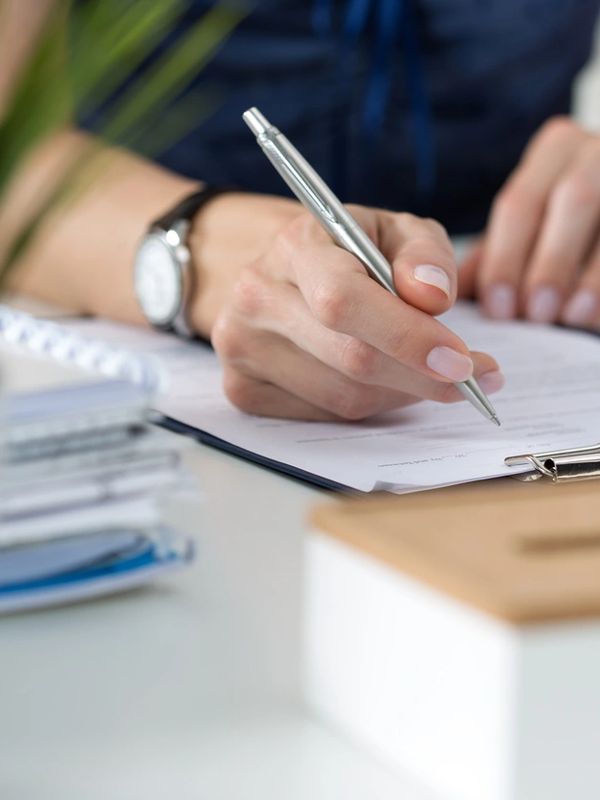 Close-up of a person writing on a clipboard with a silver pen.