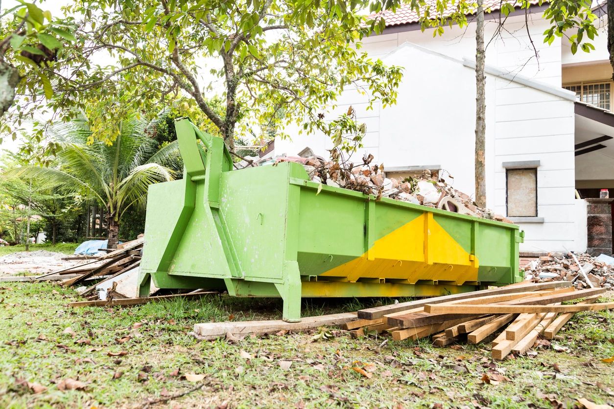 Green and yellow dumpster filled with construction debris in a yard.