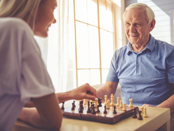Elderly man and young woman playing chess together indoors.