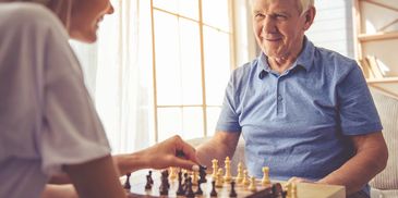 A young woman and an elderly man playing chess indoors.