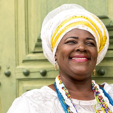 A Black African woman smiling in front of an old door wearing many necklaces