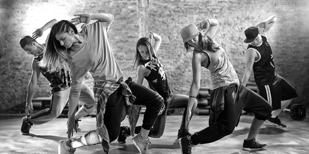 Five dancers striking a dynamic pose in a studio with a brick wall.