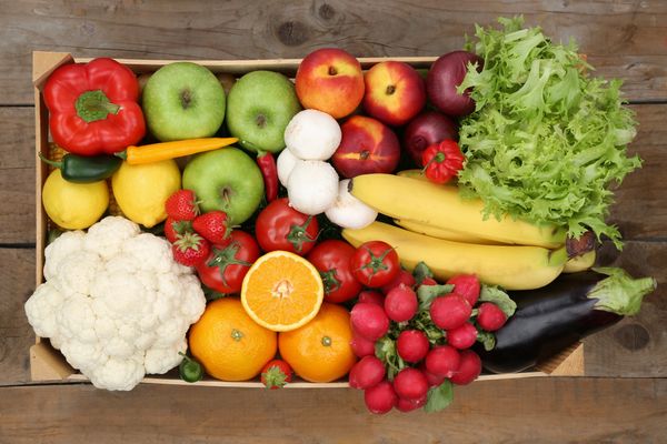 A colorful assortment of fresh fruits and vegetables in a wooden crate.