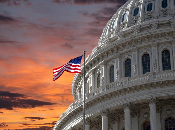 American flag waving near a domed government building at sunset.