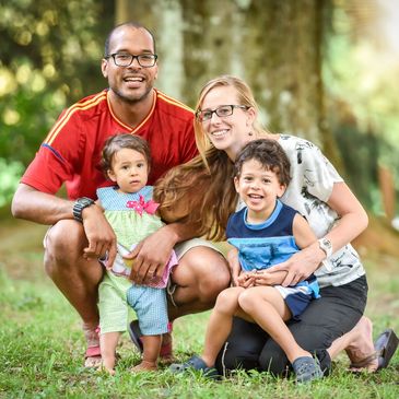 A happy family of four posing outdoors in a park.