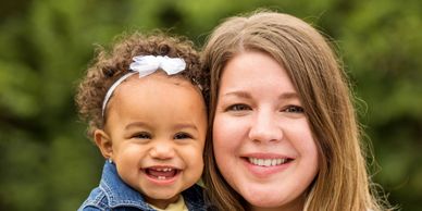 Smiling woman holding smiling baby, looking straight at the camera.