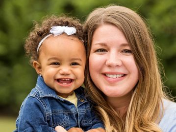 Smiling mother holding her happy toddler outdoors.