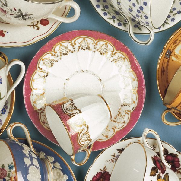 A collection of colorful vintage tea cups and saucers with floral and gold designs.