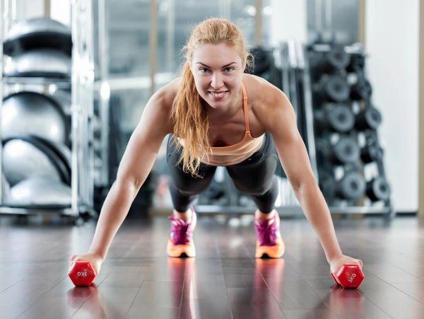 Woman doing push-ups holding red dumbbells in a gym.