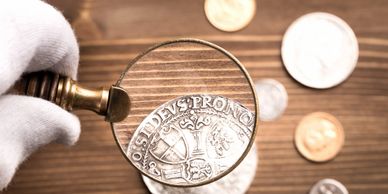 Magnifying glass enlarges details on an antique coin held with white gloves.