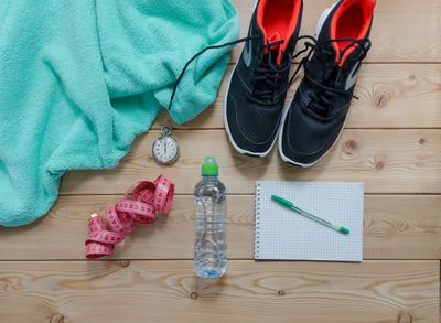 Running shoes, pen and paper, water bottle, measuring tape, and stop watch on a hardwood floor