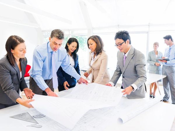 A diverse group of professionals reviewing architectural blueprints in a bright office.