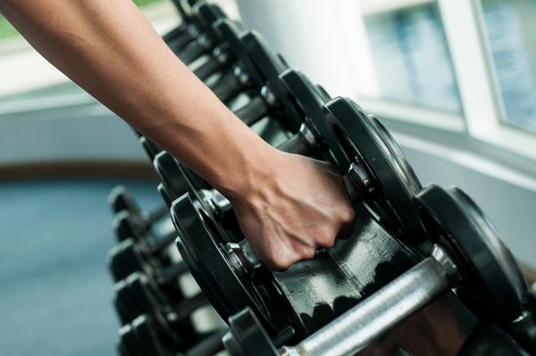 Hand grabbing a dumbbell in a gym.