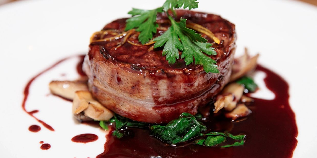 Gourmet steak wrapped in bacon with herbs and red wine sauce.