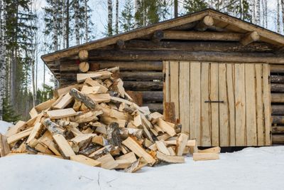Pile of chopped firewood beside a wooden cabin in snowy forest.