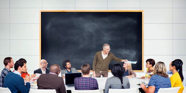 A diverse group of people in a meeting around a blackboard. 