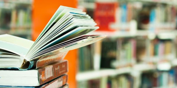 Open book resting on a stack of books in a library.