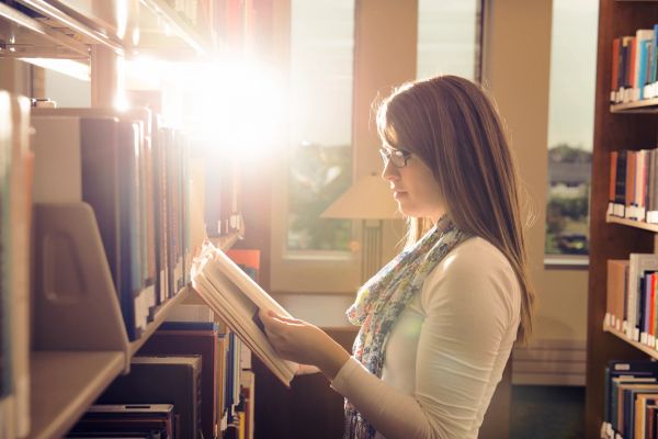 Woman reading a book in a sunlit library.
