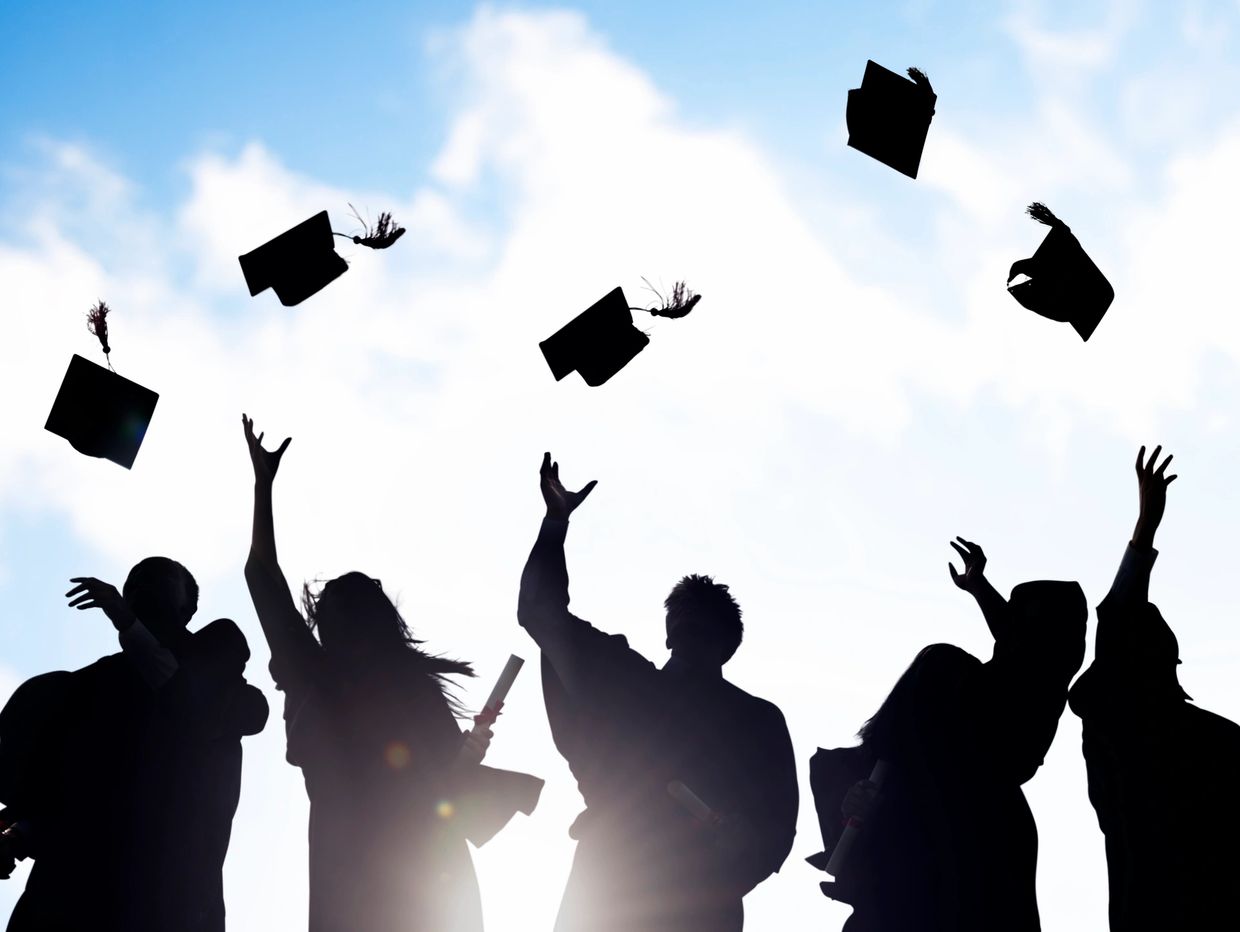 Graduates joyfully toss caps into the air under a bright sky.