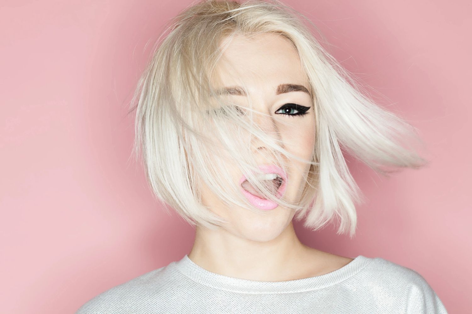 blonde hair woman with black eyeliner and white t shirt on a pink background