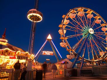 Brightly lit amusement park rides at night with people enjoying the scene.