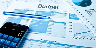 A pile of budget, financial and operational reports on a table with a calculator and pen.