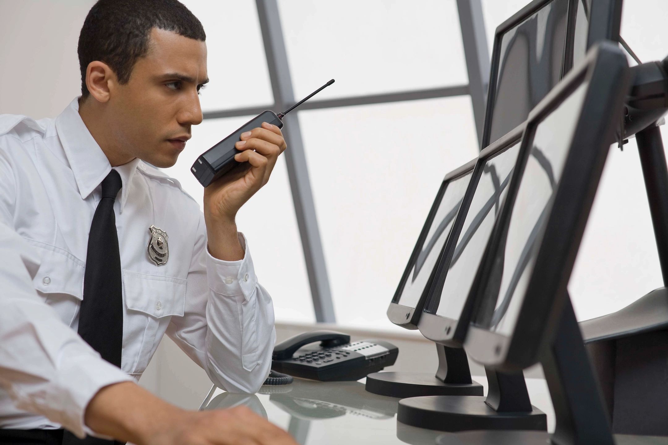 A security man talking on walkie-talkie and watching footage on monitor