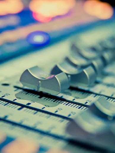 Close-up of sound mixing console sliders with colorful blurred lights.