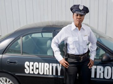 Security officer standing confidently beside a marked security patrol car.