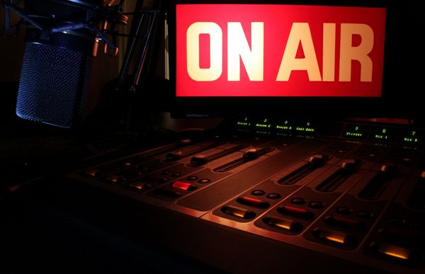 Radio studio setup with microphone and 'ON AIR' sign glowing.