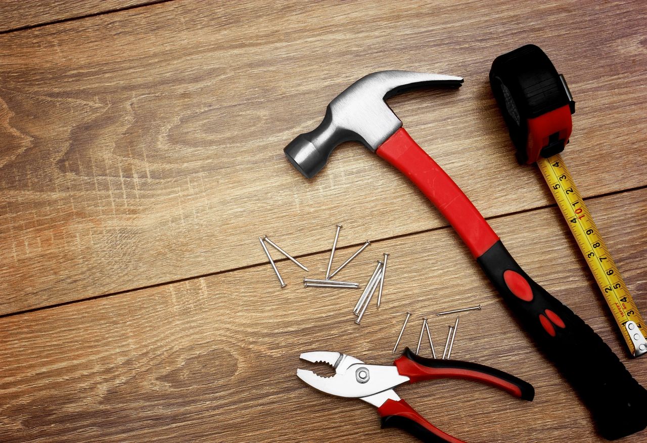 A red measuring tape, red hammer, nails and red wrench, lay on the floor.