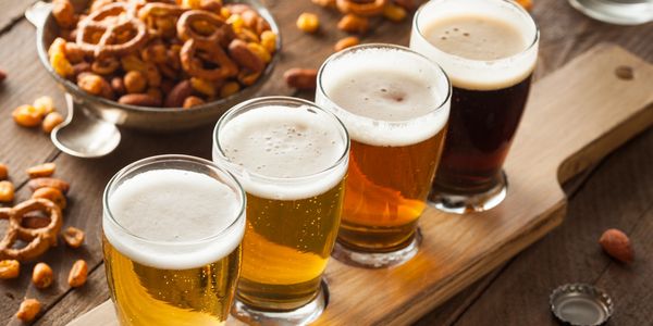 Four glasses of different beers with snacks on a wooden board.