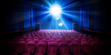 Empty movie theater seats with bright projector light.