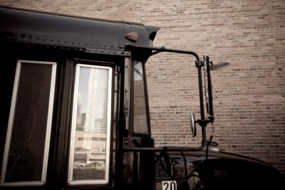 Side view of a black bus parked by a brick wall.