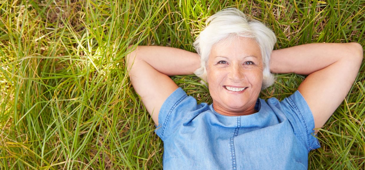 Smiling lady with white hair lying down on green grass 