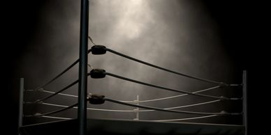 Empty boxing ring under spotlight with smoky background.