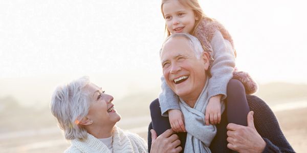 Grandfather holding a young girl on his shoulders while the grandmother stands next to them smiling