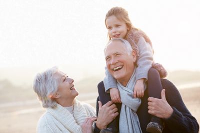 Color photo of elderly couple walking along a beach, with a little girl on the man's shoulders