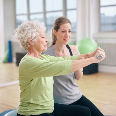 Senior woman exercising with a trainer holding weights in a fitness studio.