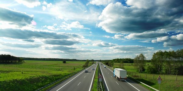Vehicles are driving on the highway surrounding green grass and clean sky.