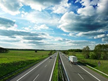 Highway cutting through green fields under a cloudy sky.