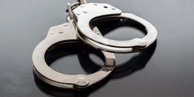 A pair of metallic handcuffs on a reflective surface.