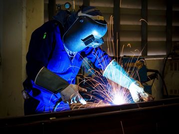 A welder in protective gear welding metal with sparks flying.