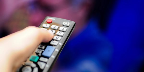 A hand pressing a button on a TV remote. 