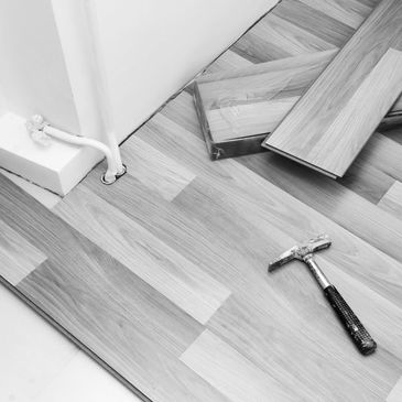 Wooden flooring being installed with a hammer and planks near a wall socket.