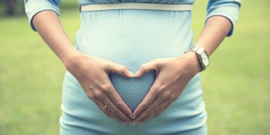 Pregnant woman forming a heart shape with hands on belly.
