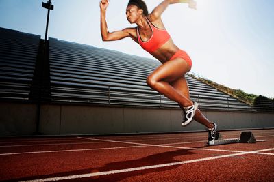 Athlete sprinting off starting blocks on a track in bright sunlight.